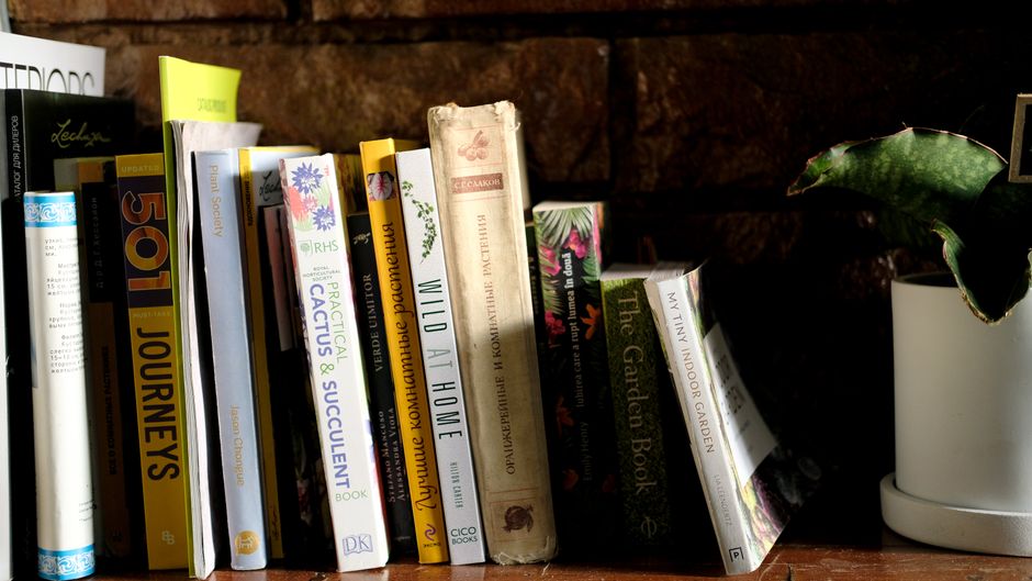 A close-up view of a wooden bookshelf with a collection of gardening and outdoor-related books arranged upright, including titles on landscape design, vegetable gardening, and pruning, with some books